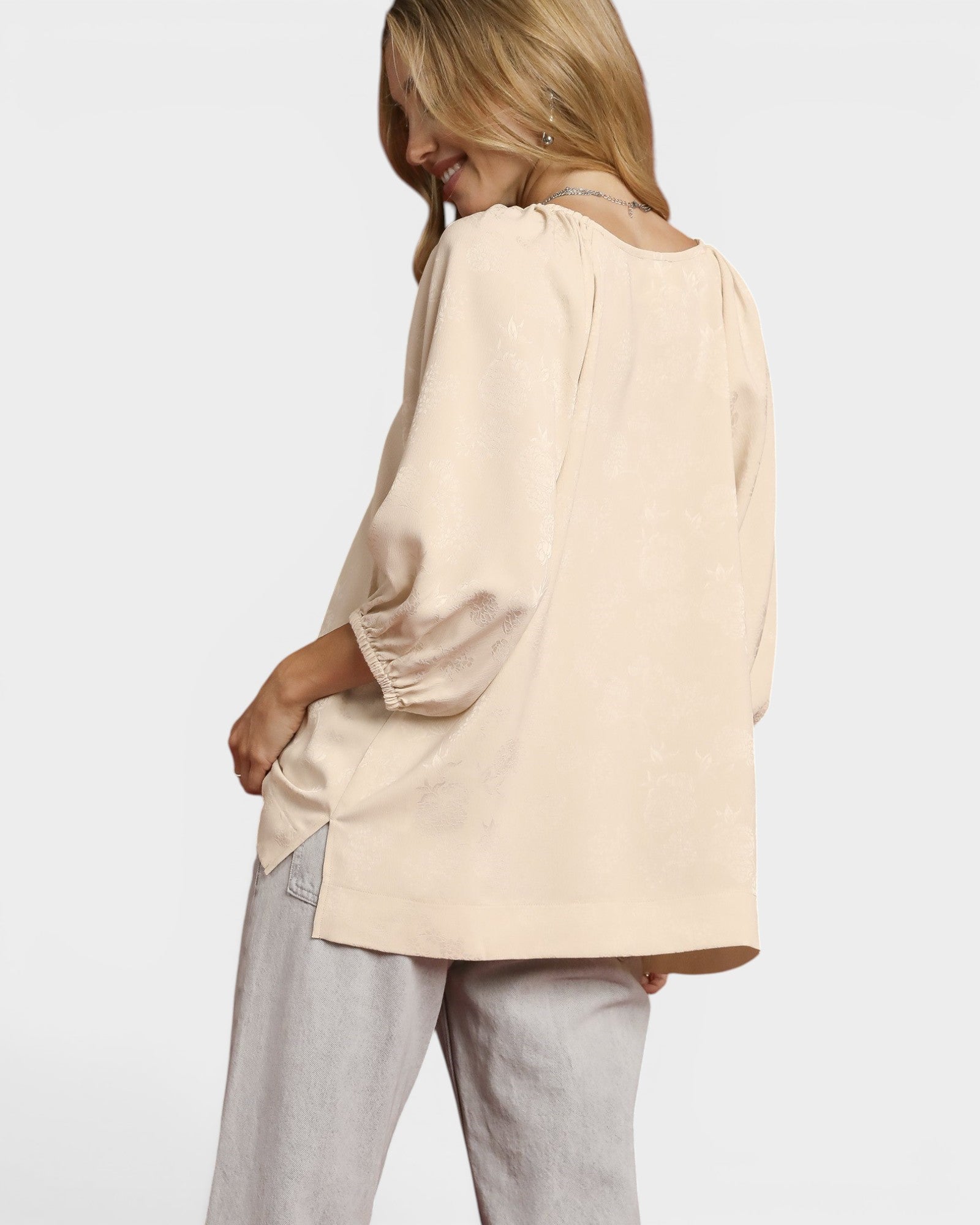 Woman wearing a beige blouse and light gray pants on a white background
