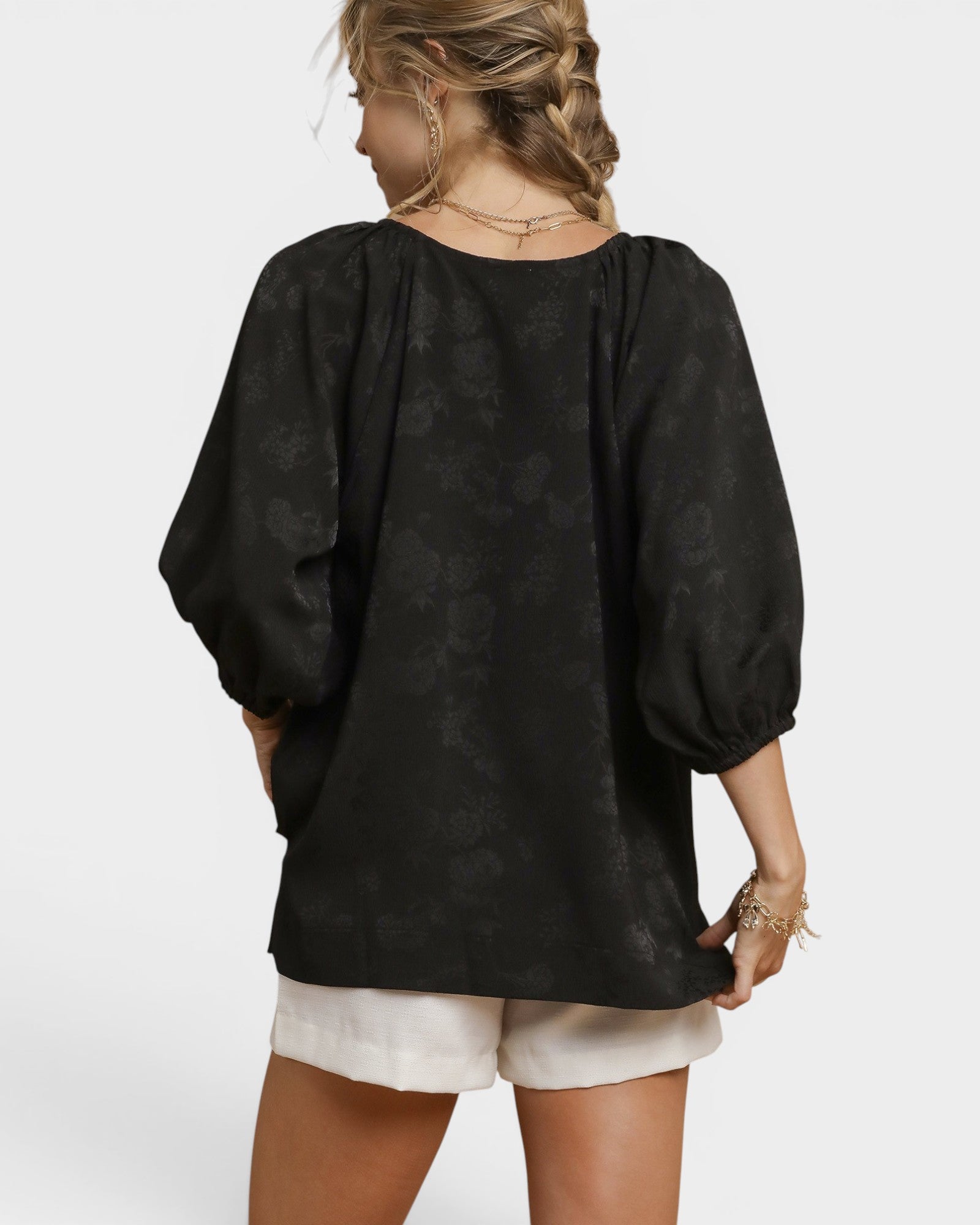 Person wearing a black floral blouse with white shorts on a plain background