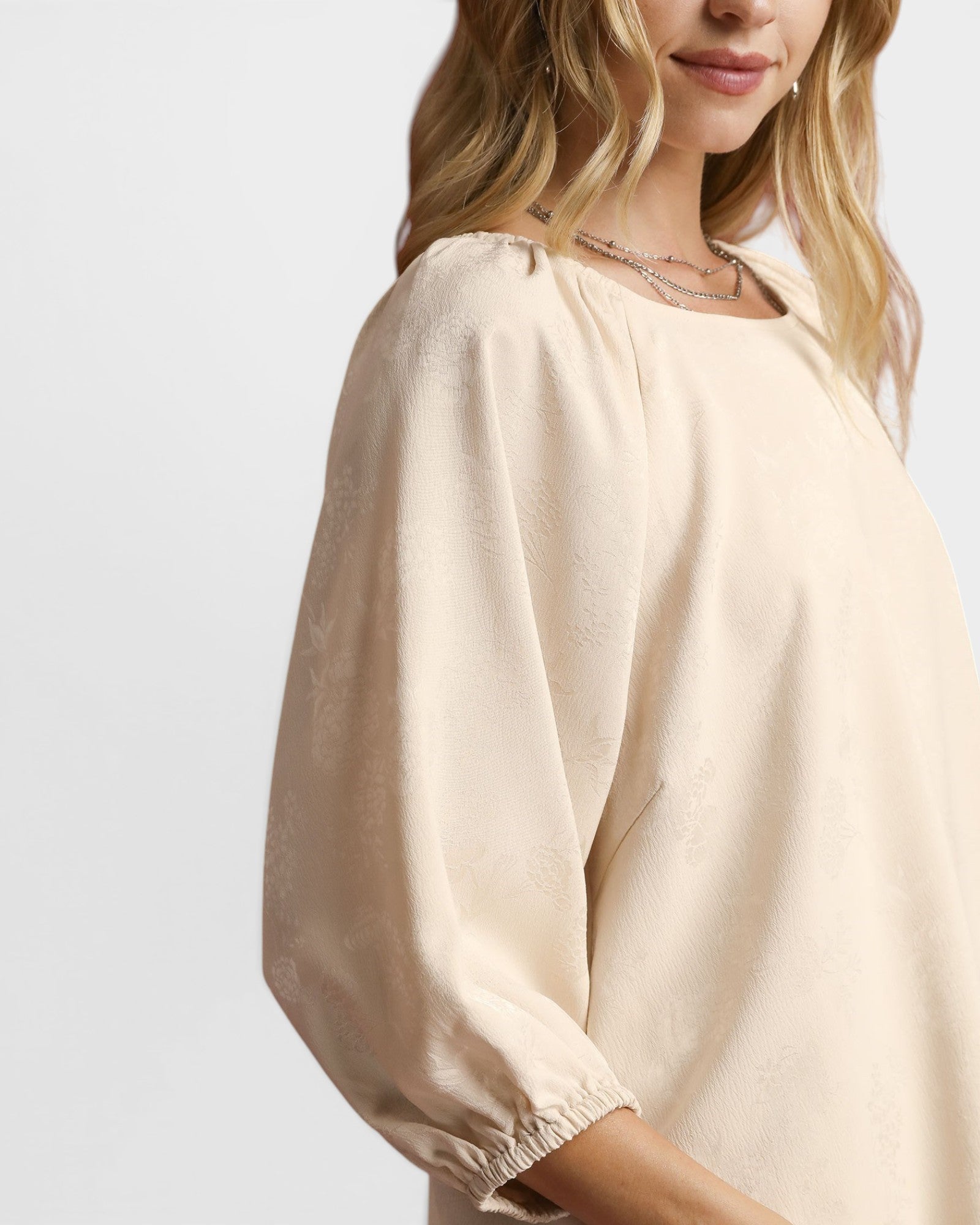 Woman wearing a beige blouse against a plain background