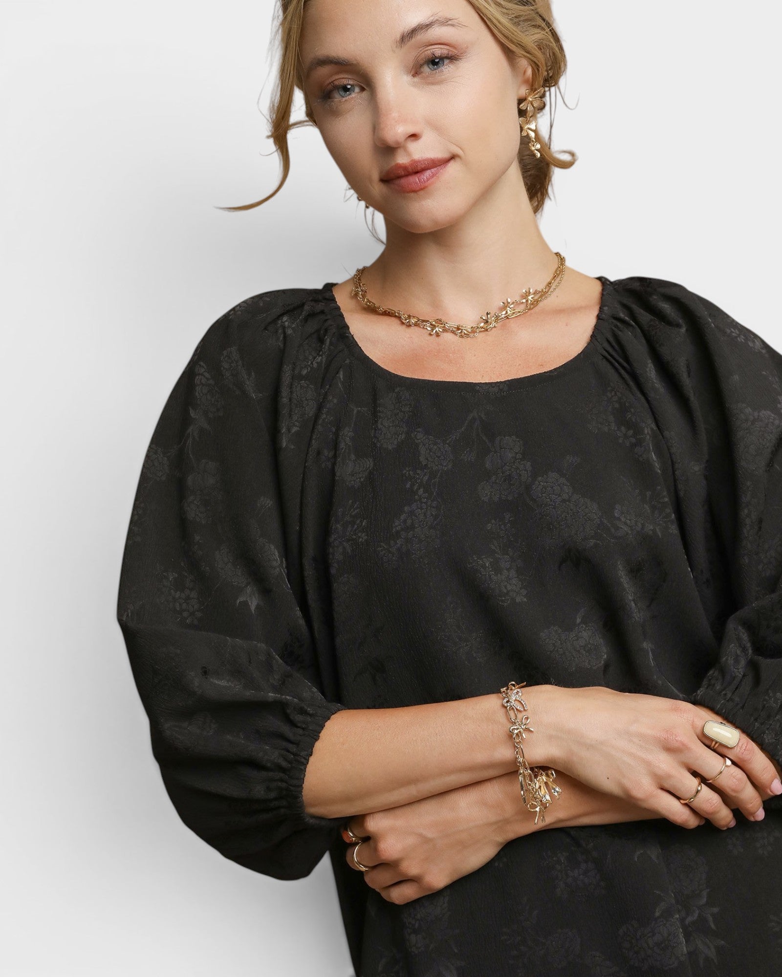 Woman wearing a black blouse with gold jewelry against a white background