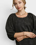 Woman wearing a black blouse with gold jewelry against a white background
