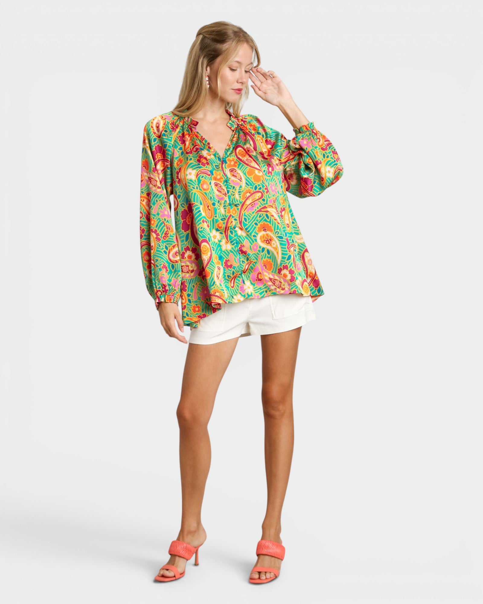 Woman wearing a colorful patterned blouse and white shorts on a white background