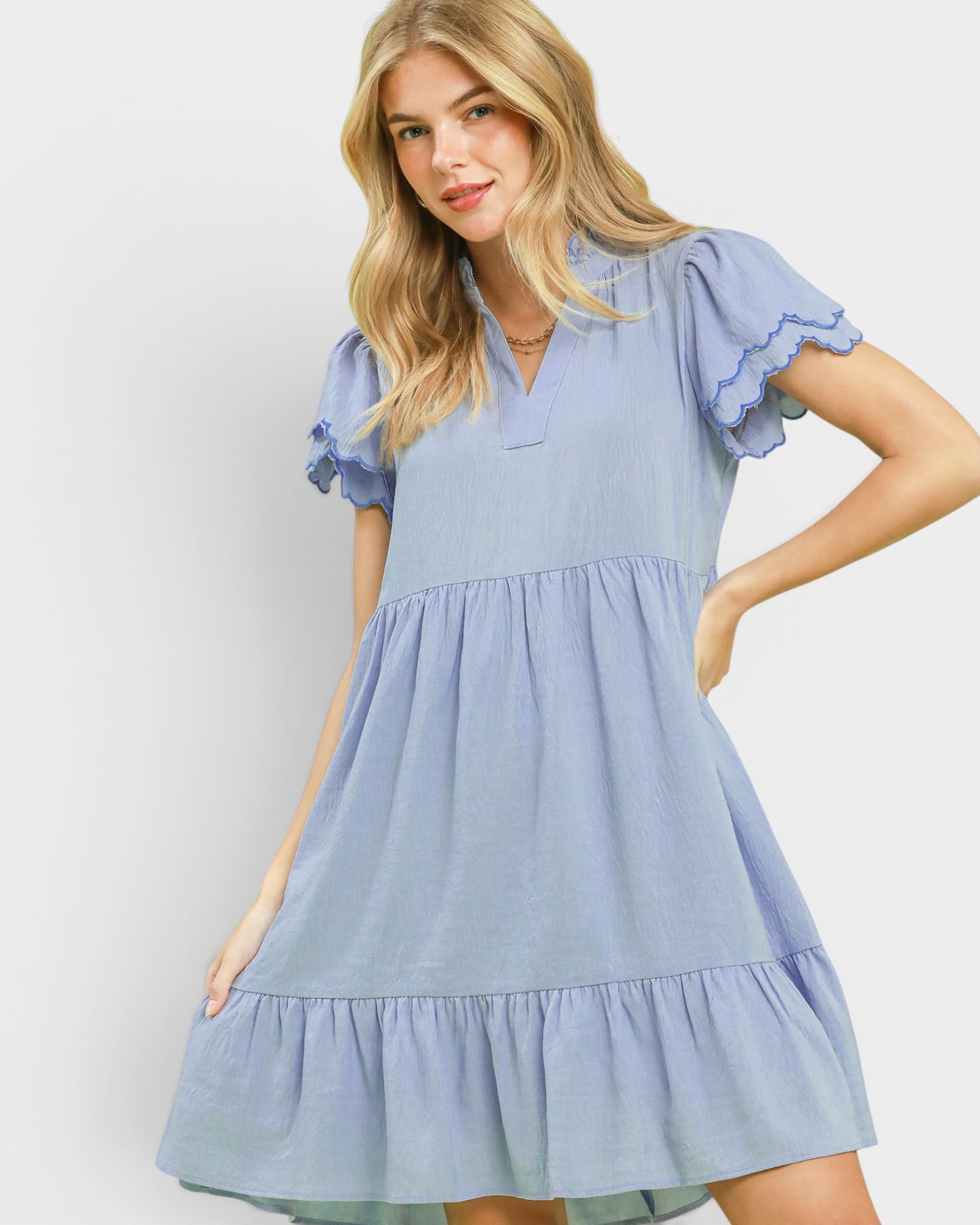 Woman wearing a light blue dress with ruffled sleeves and bottom hem on a plain background
