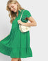 Woman wearing a green dress holding a white handbag on a light gray background
