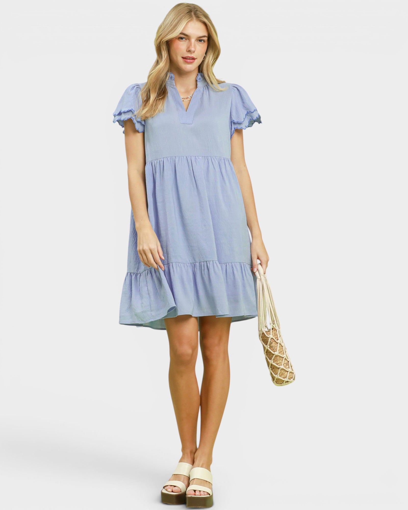 Woman wearing a light blue dress holding a beige bag on a white background