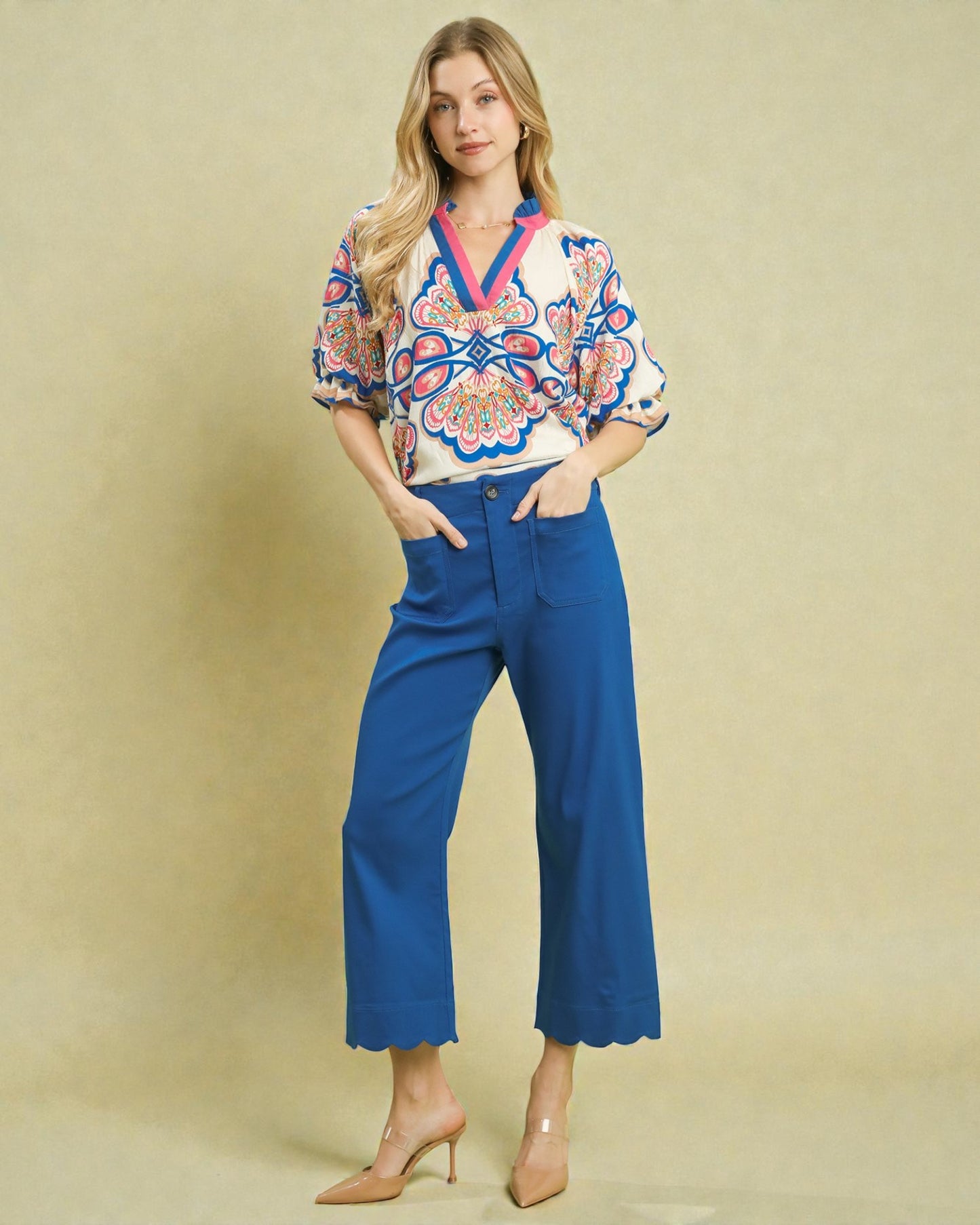 Woman wearing a colorful blouse and blue pants against a beige background