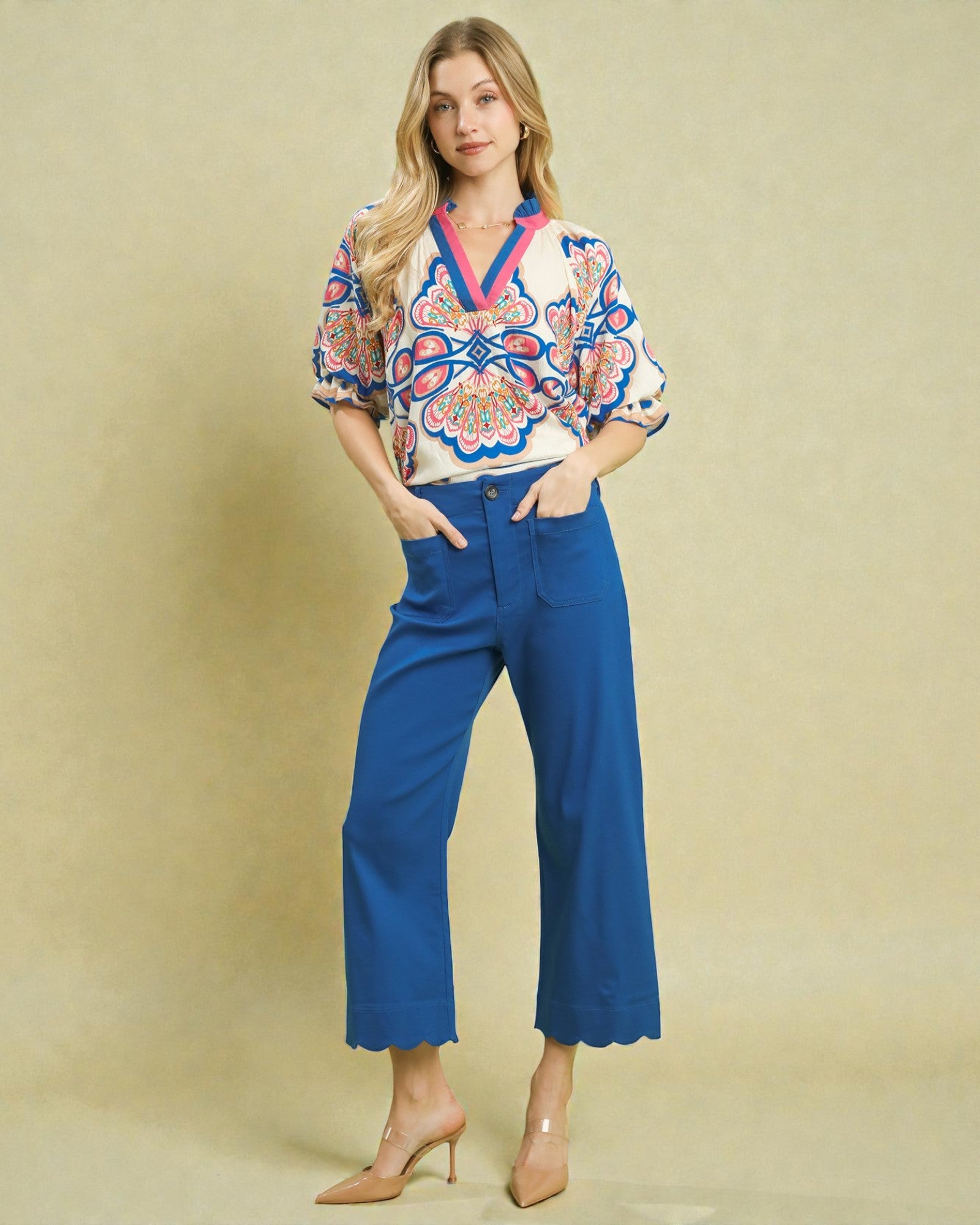 Woman wearing a colorful blouse and blue pants against a beige background