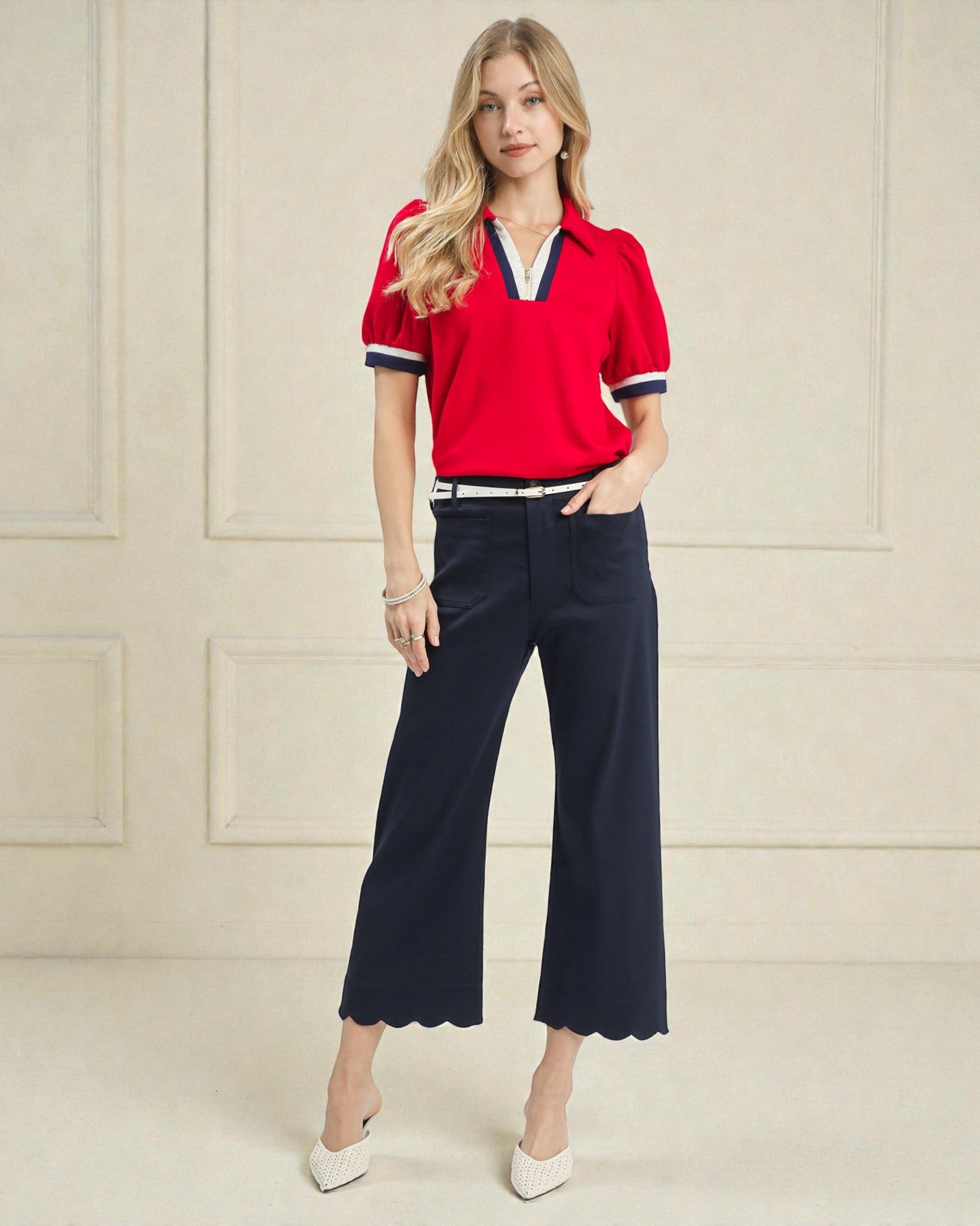 Woman wearing a red polo shirt and navy pants against a beige wall.