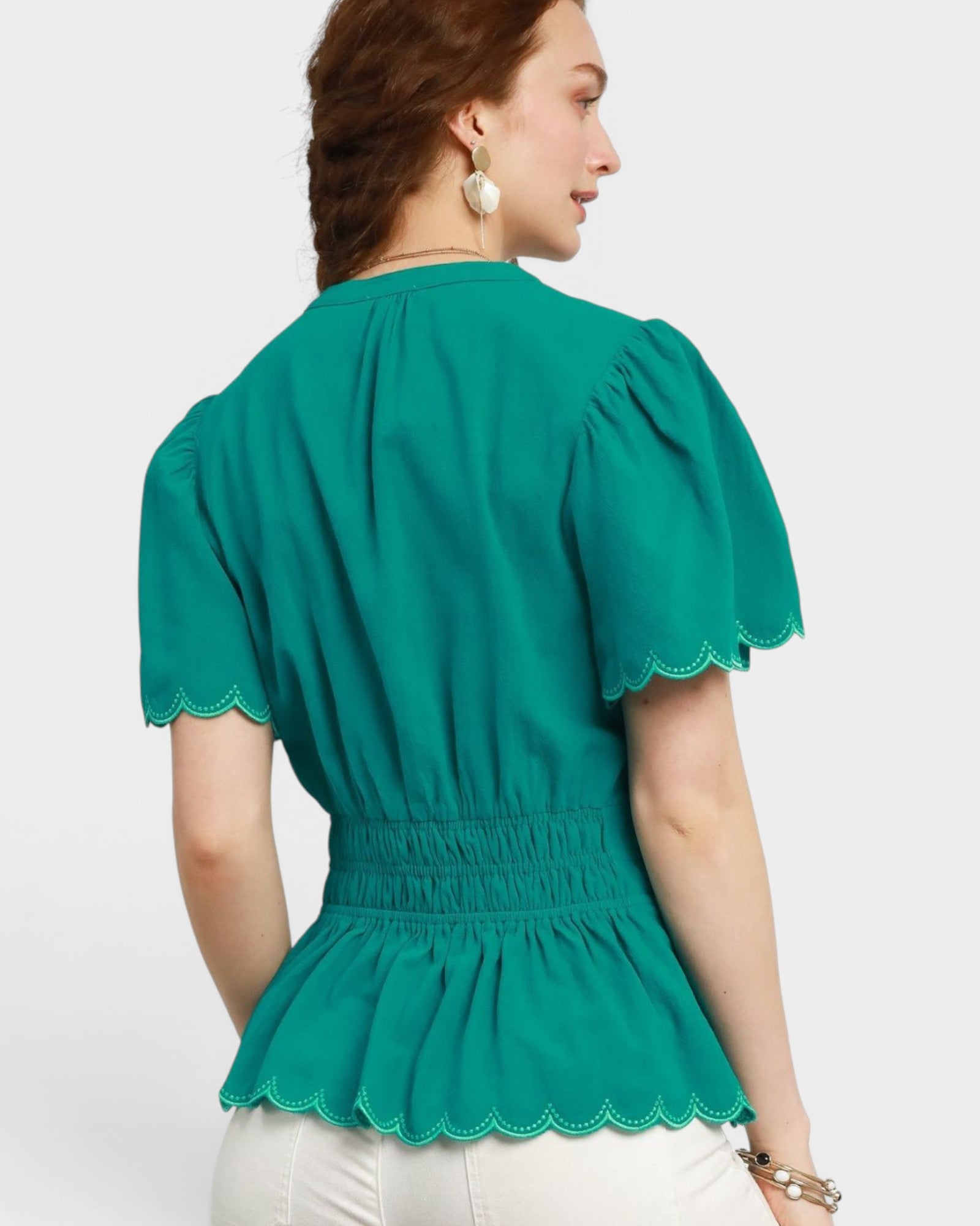 Woman wearing a green blouse with scalloped trim on a white background