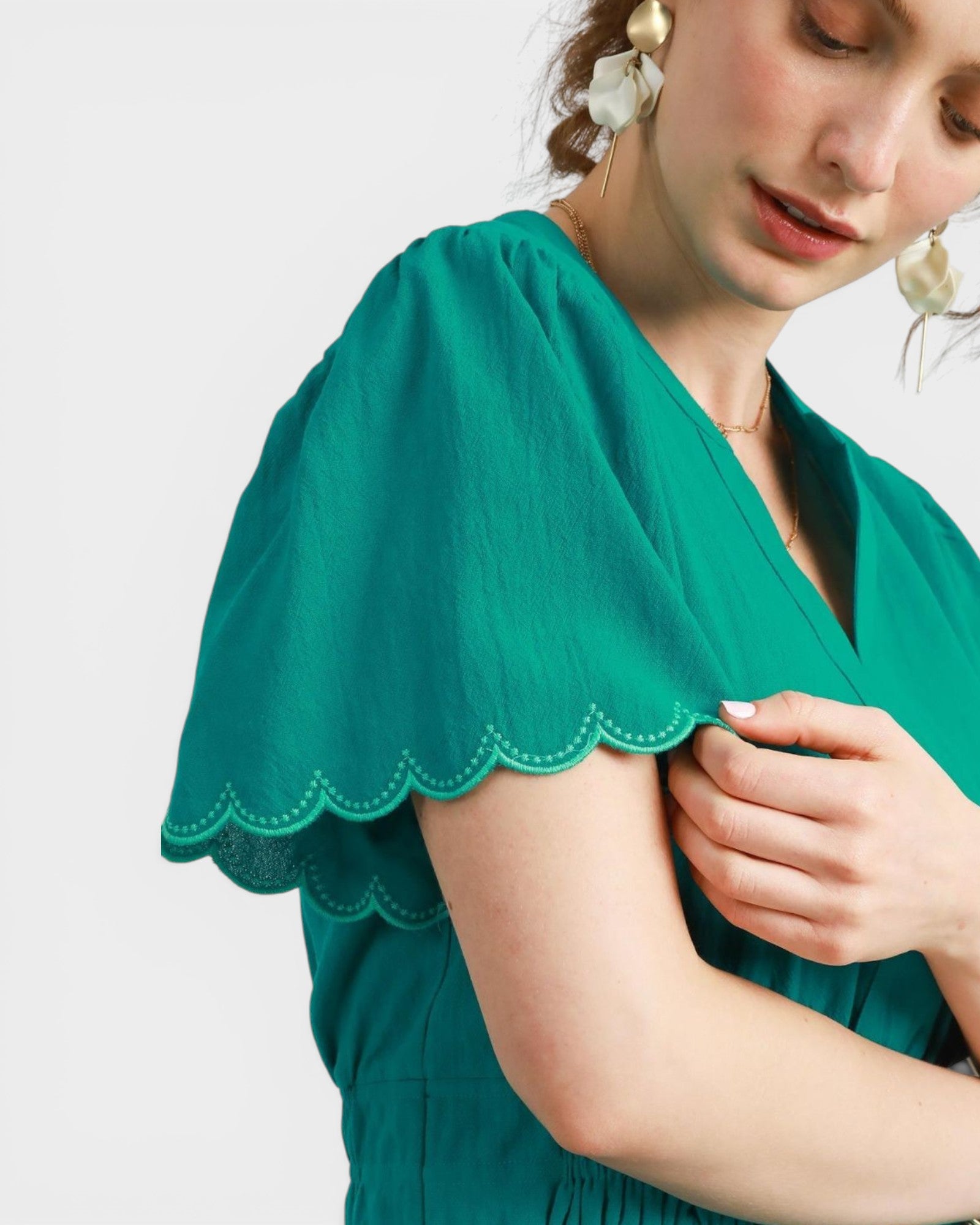 Green blouse with scalloped trim worn by a person on a white background