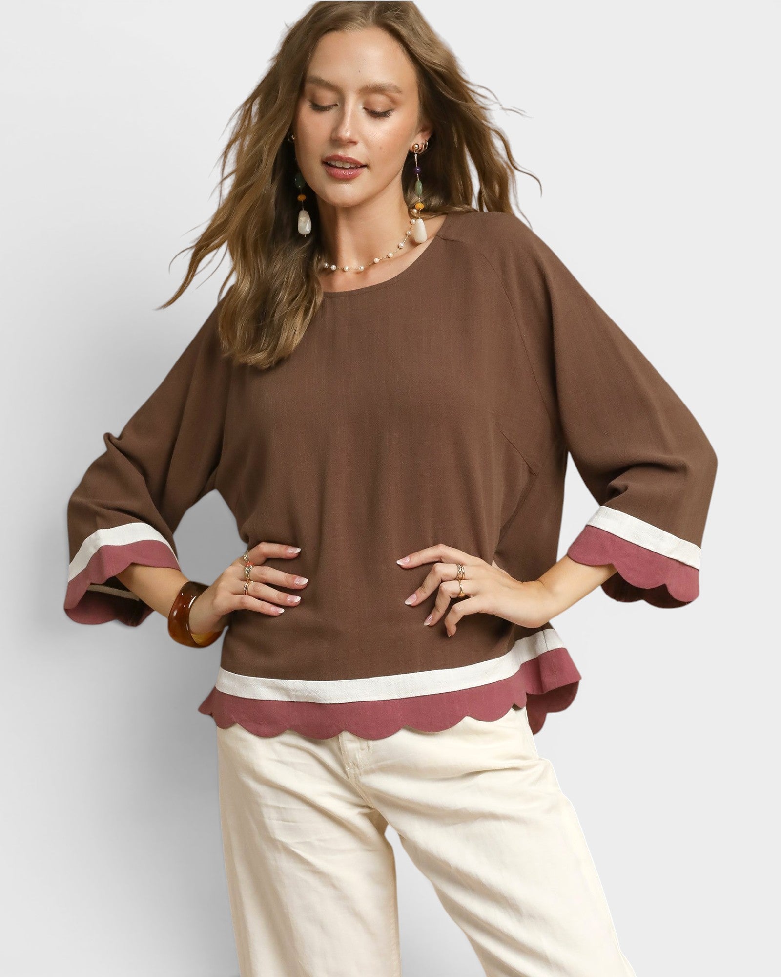Woman wearing a brown blouse with maroon cuffs and trim on a white background