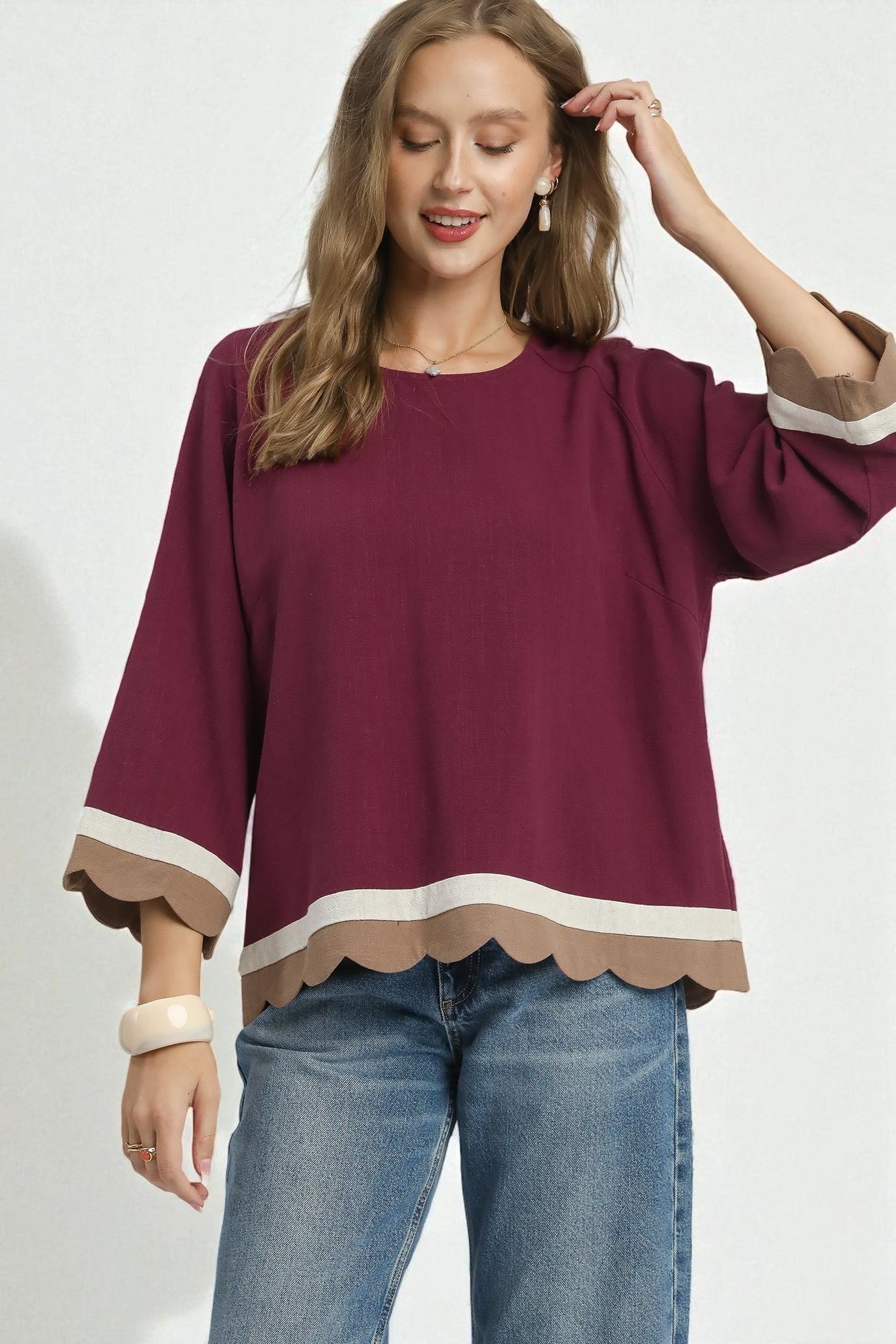 Woman wearing a burgundy blouse with scalloped cuffs and hem on a white background