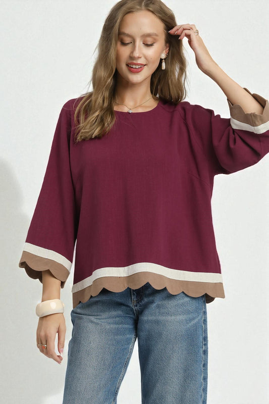 Woman wearing a burgundy blouse with scalloped cuffs and hem on a white background