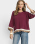 Woman wearing a burgundy blouse with scalloped hem and blue jeans on a white background