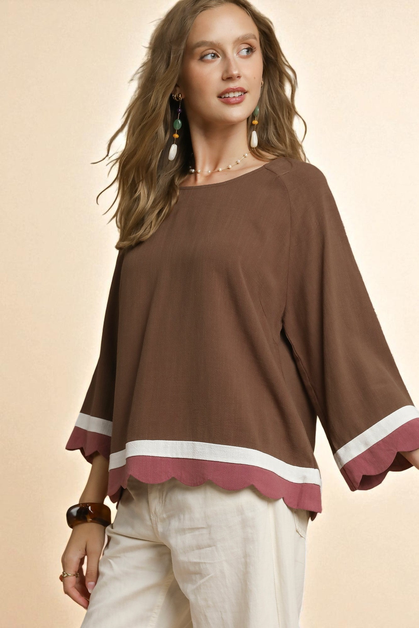Woman wearing a brown blouse with scalloped edges on a beige background
