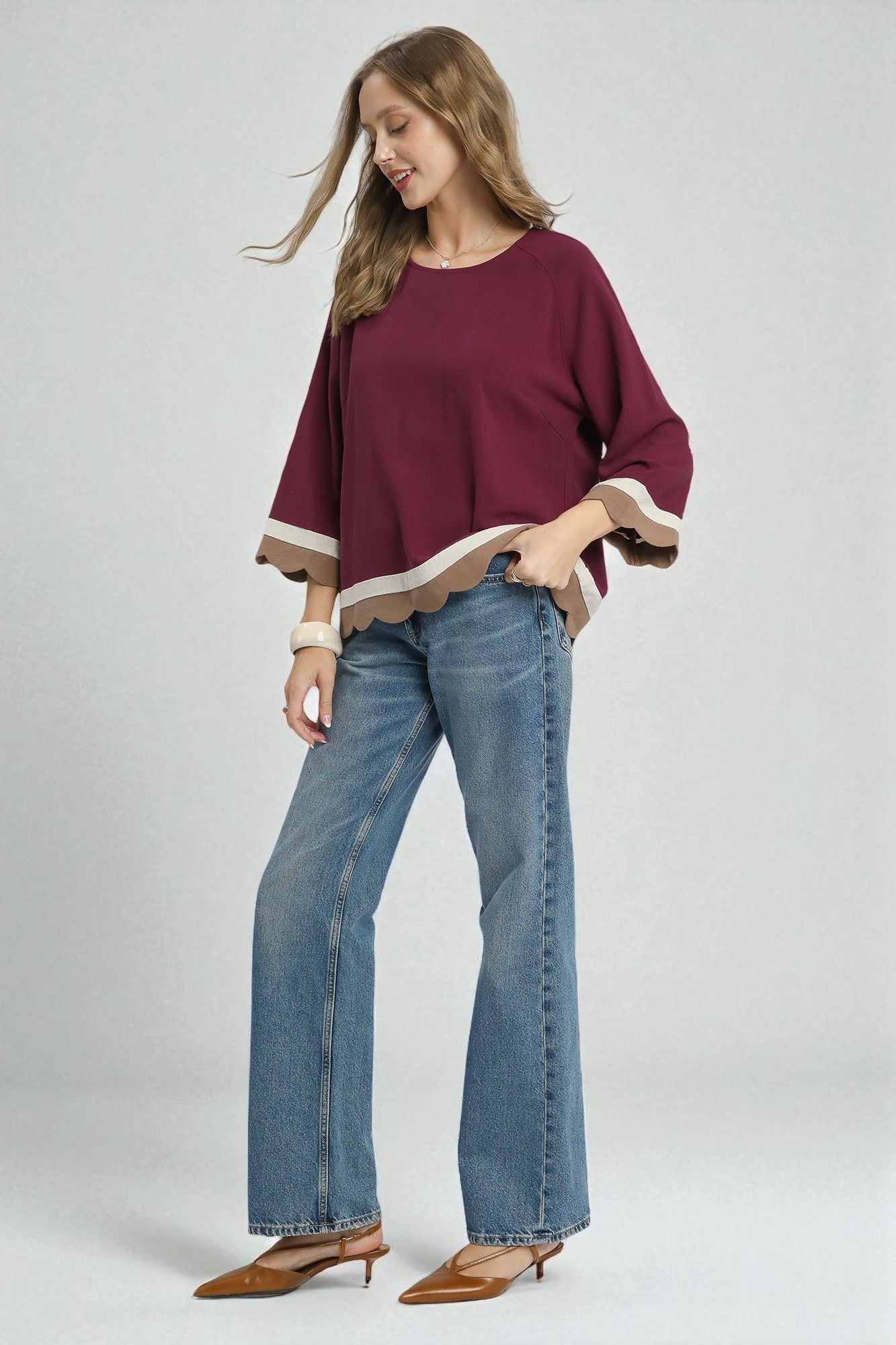 Woman wearing a burgundy top and blue jeans on a white background
