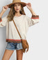 Woman wearing a beige sweater with brown and red accents, denim shorts, and a tan hat on a light gray background.