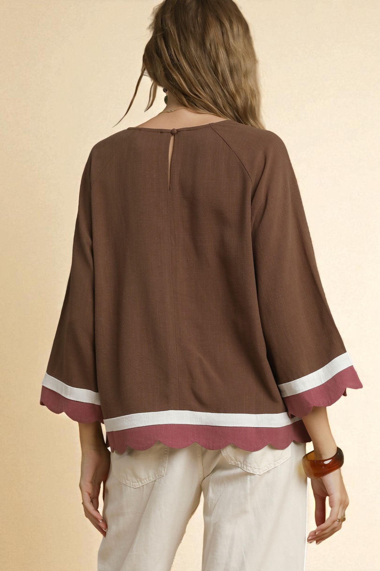 Brown blouse with white and red trim worn by a person on a beige background