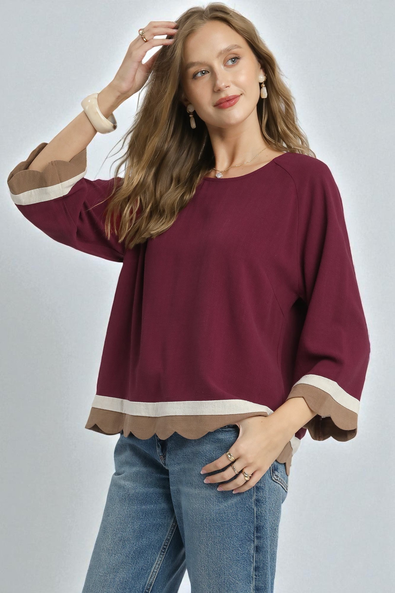 Woman wearing a burgundy top with scalloped hem and blue jeans on a plain background