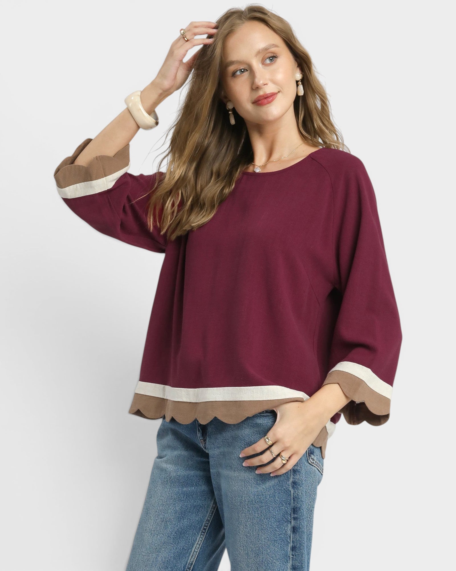 Woman wearing a burgundy top with scalloped hem and blue jeans on a white background