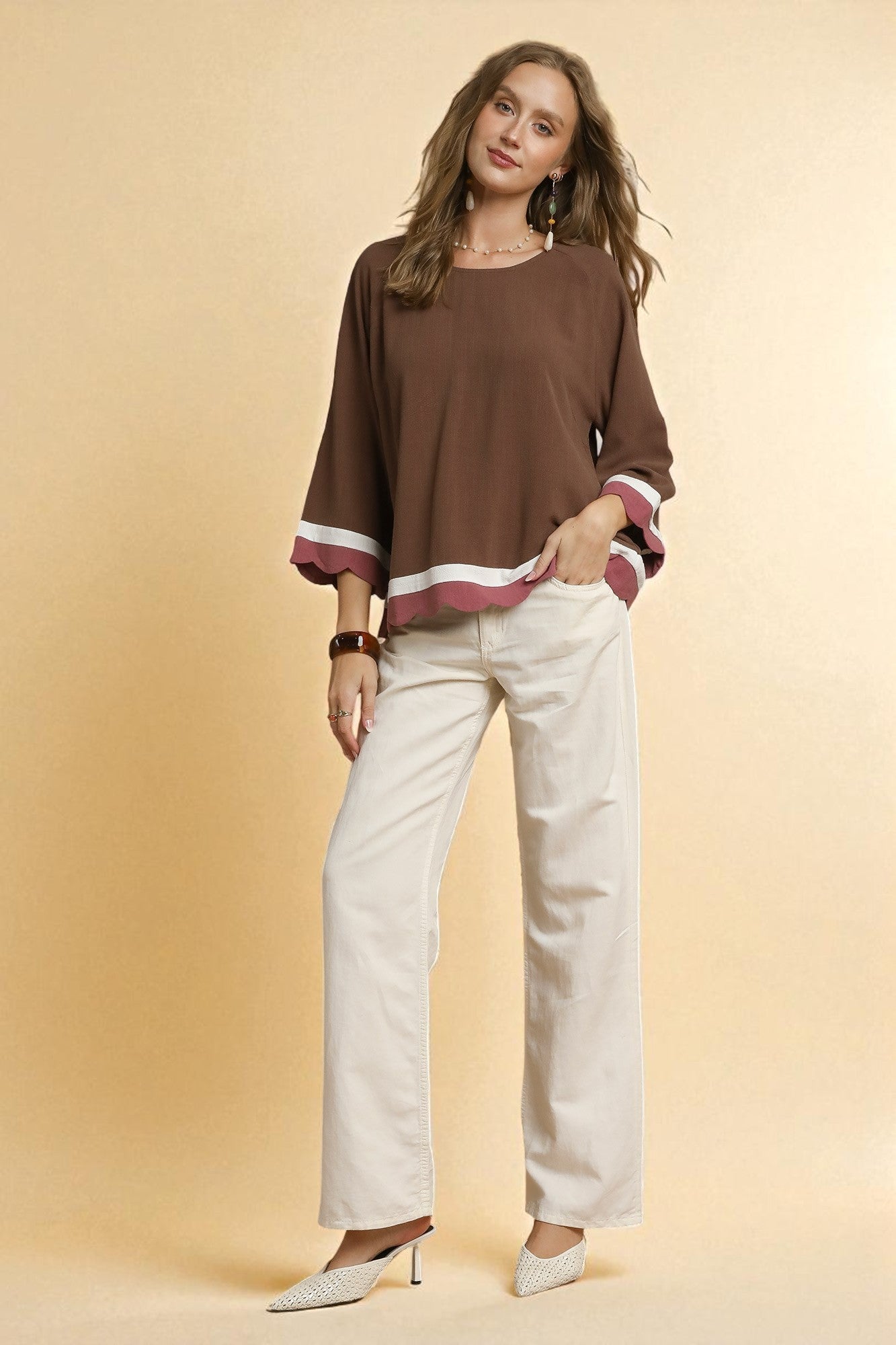 Woman wearing a brown top with white pants on a beige background