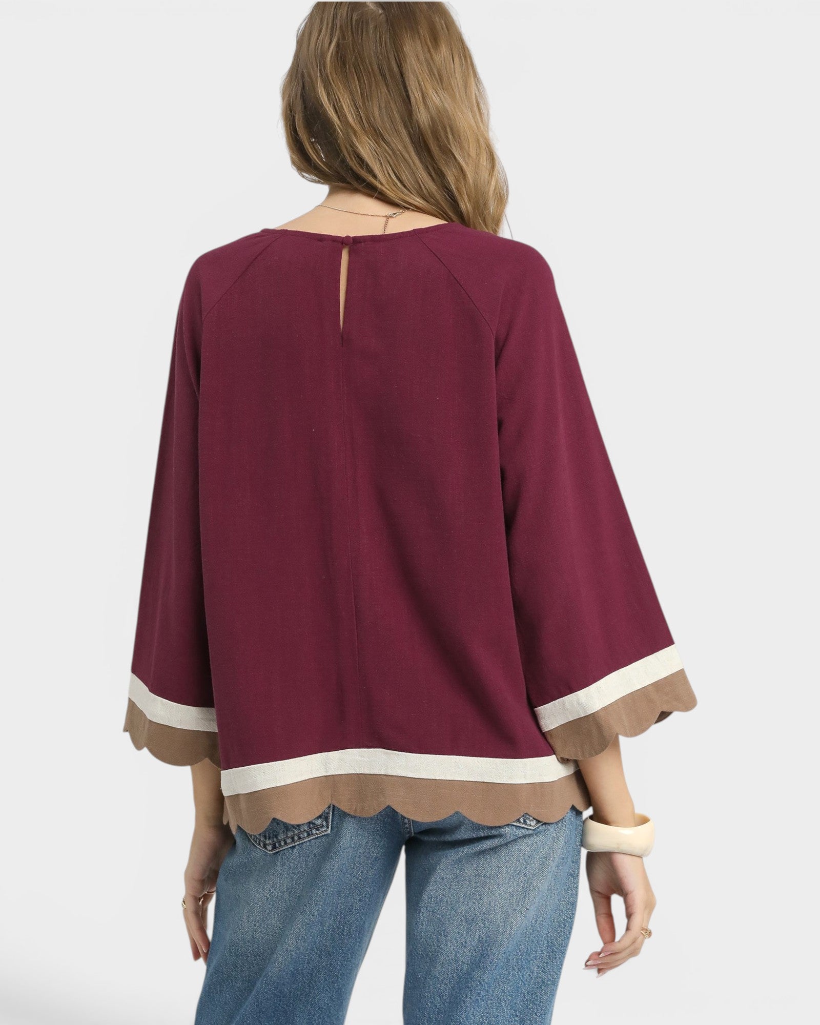 Maroon blouse with scalloped hem and cuffs worn by a person on a white background