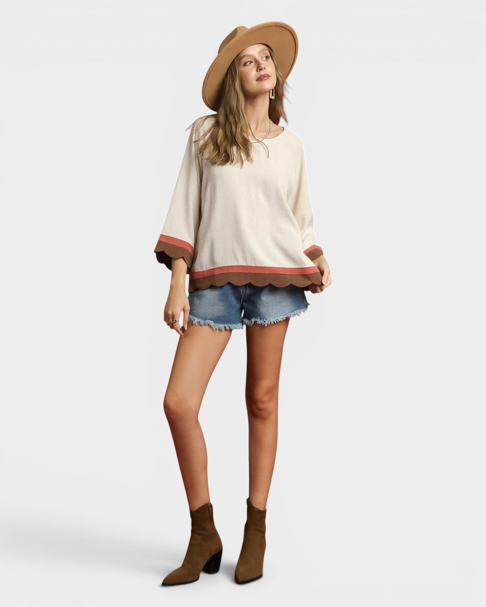 Woman wearing a beige top, denim shorts, and brown boots on a white background