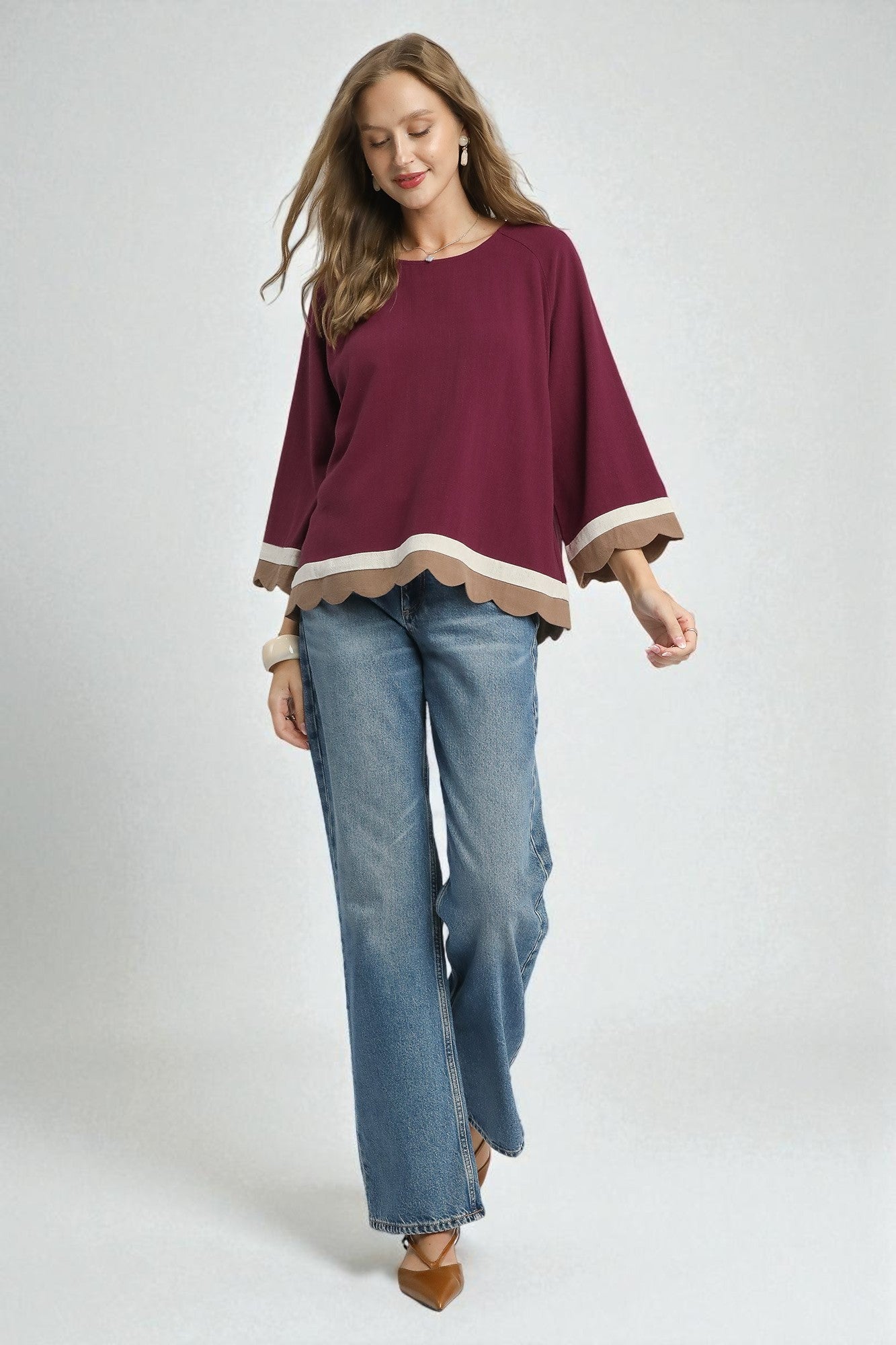 Woman wearing a burgundy top with a white trim and blue jeans on a white background