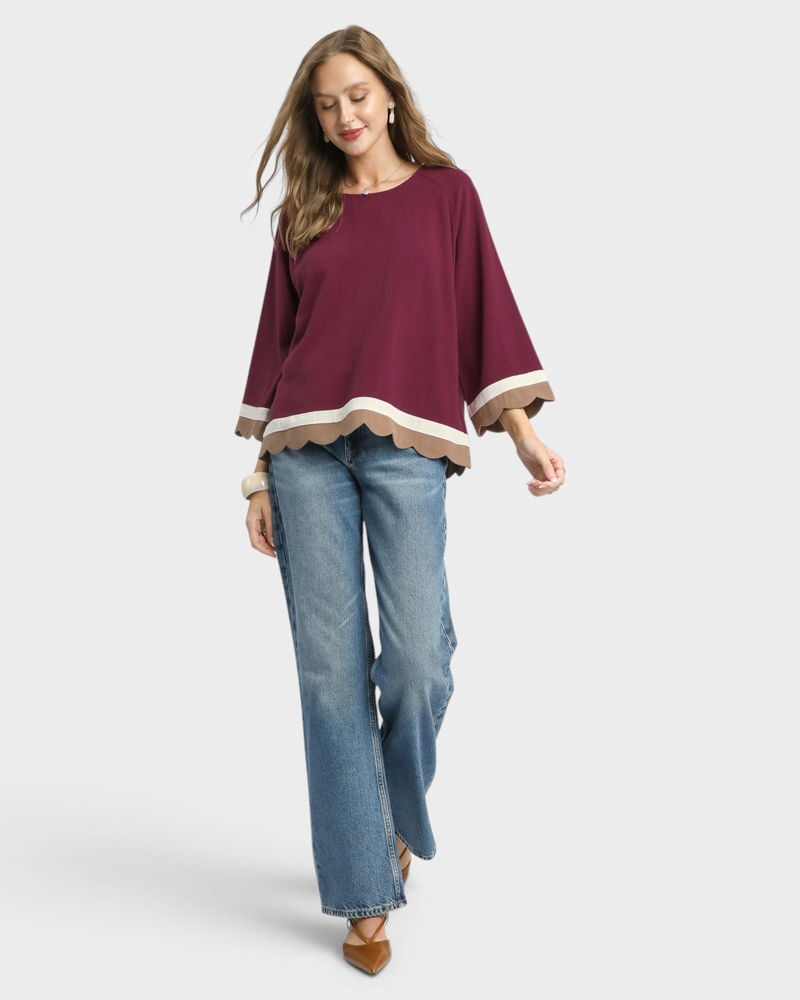 Woman wearing a burgundy top with a scalloped hem and blue jeans on a white background