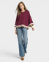 Woman wearing a burgundy top with a scalloped hem and blue jeans on a white background