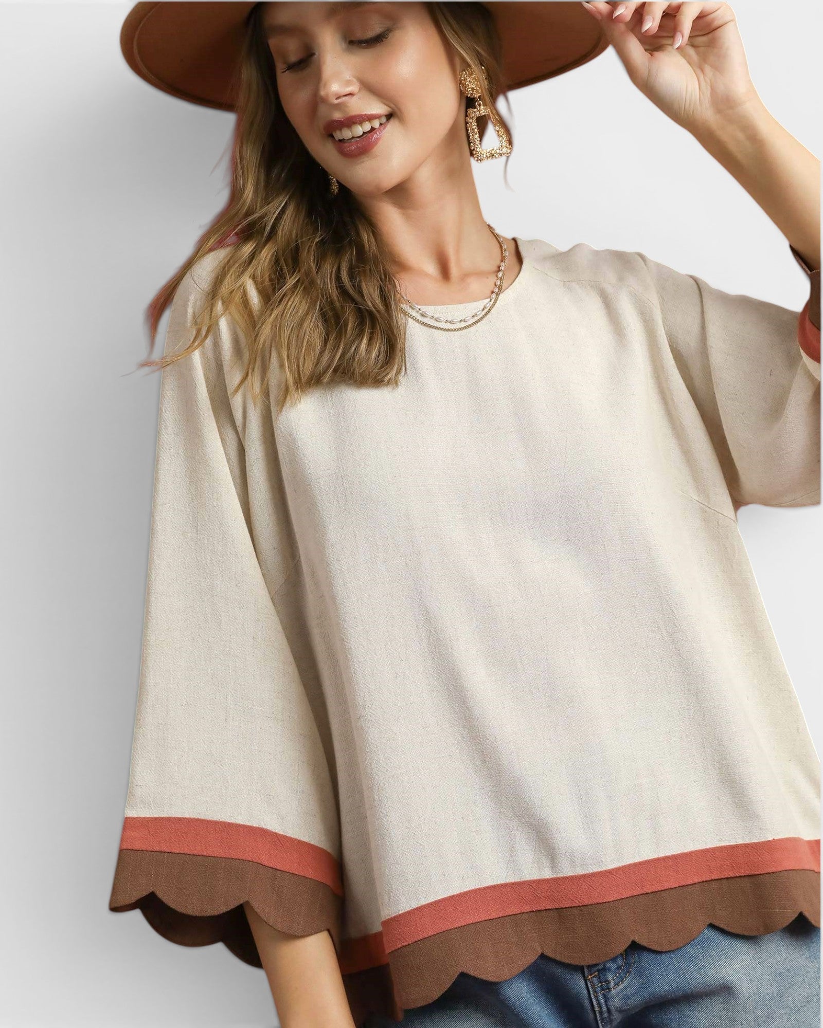 Woman wearing a beige poncho with brown trim on a plain background