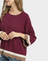 Maroon top with white and beige trim worn by a person on a light gray background