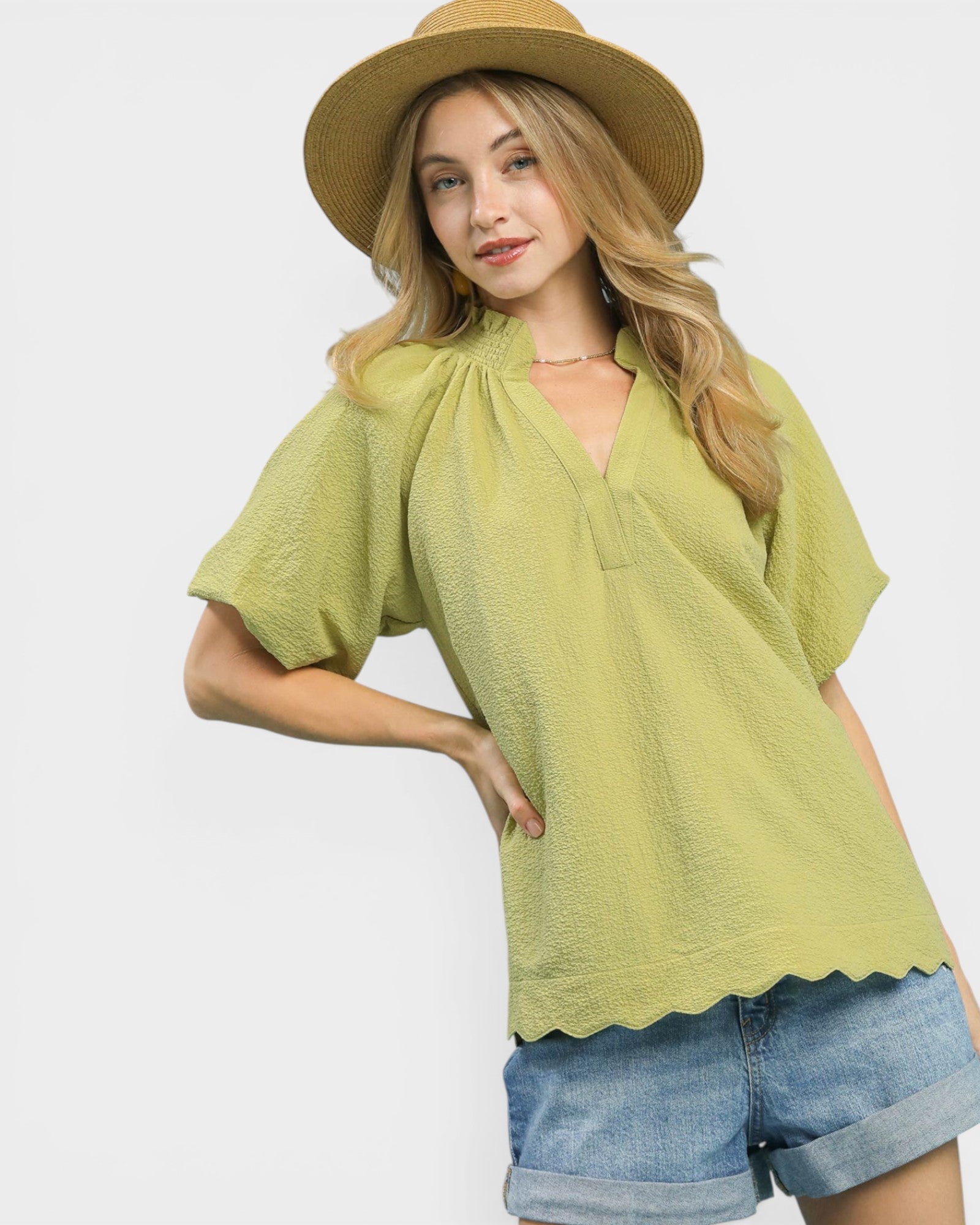 Woman wearing a green top and denim shorts with a straw hat on a white background