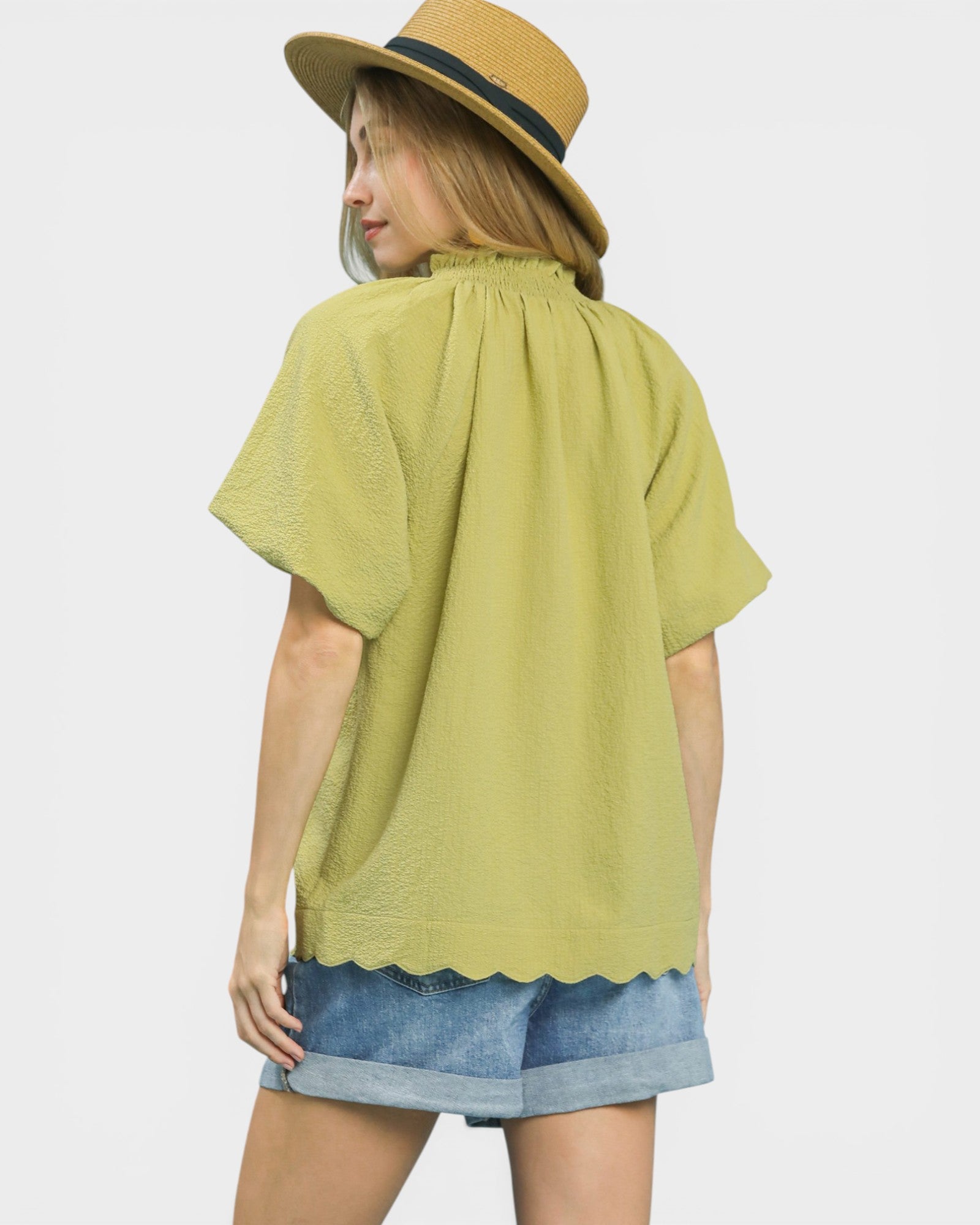 Woman wearing a green top and denim shorts with a beige hat on a white background
