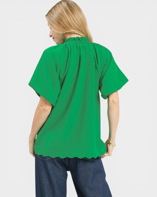 Woman wearing a green blouse with scalloped hem on a white background