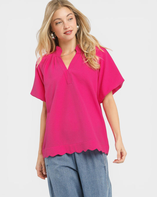 Woman wearing a bright pink blouse with scalloped hem on a white background