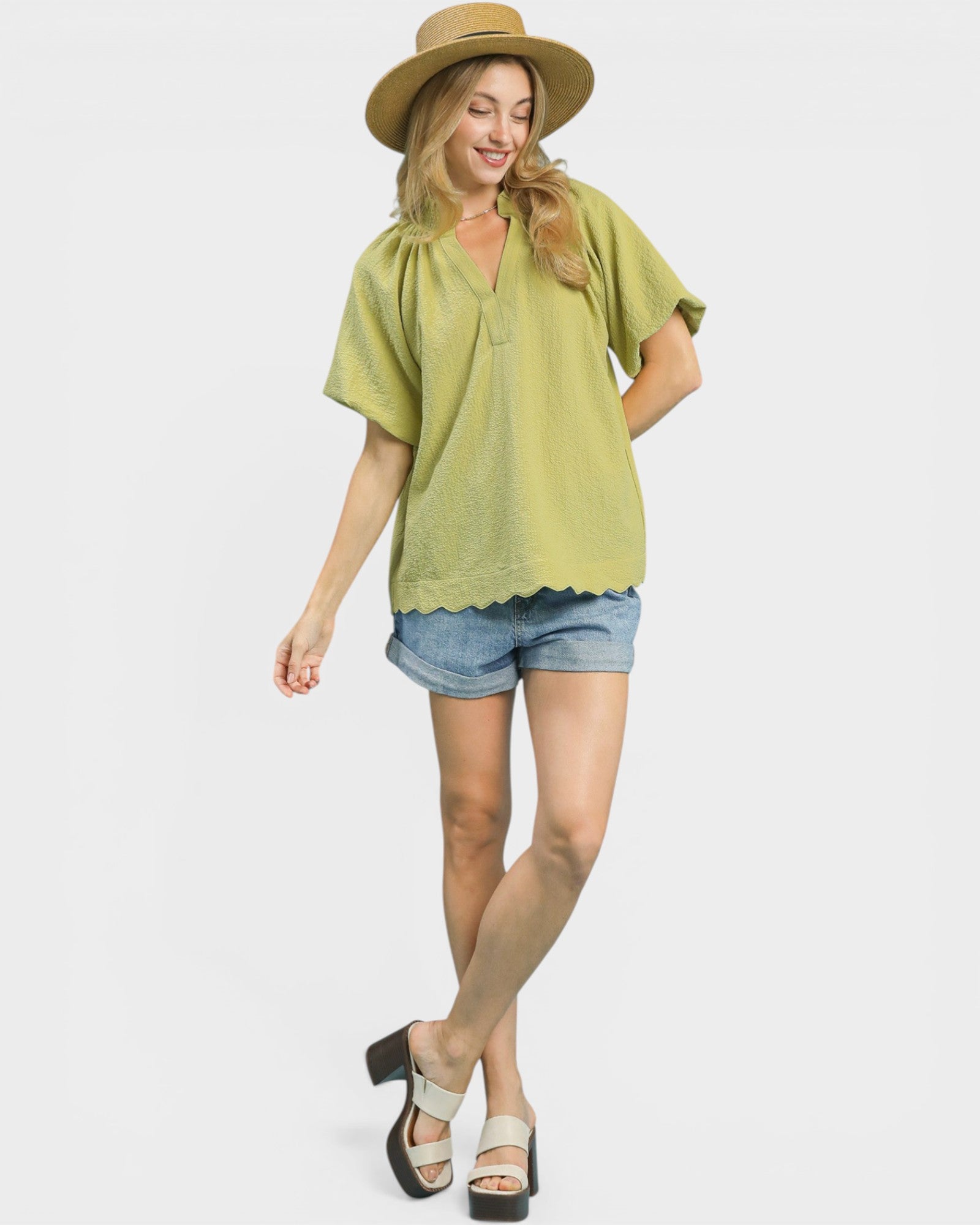 Woman wearing a green top and denim shorts with a straw hat on a white background