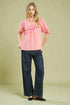 Woman wearing a pink blouse and dark blue jeans against a beige background
