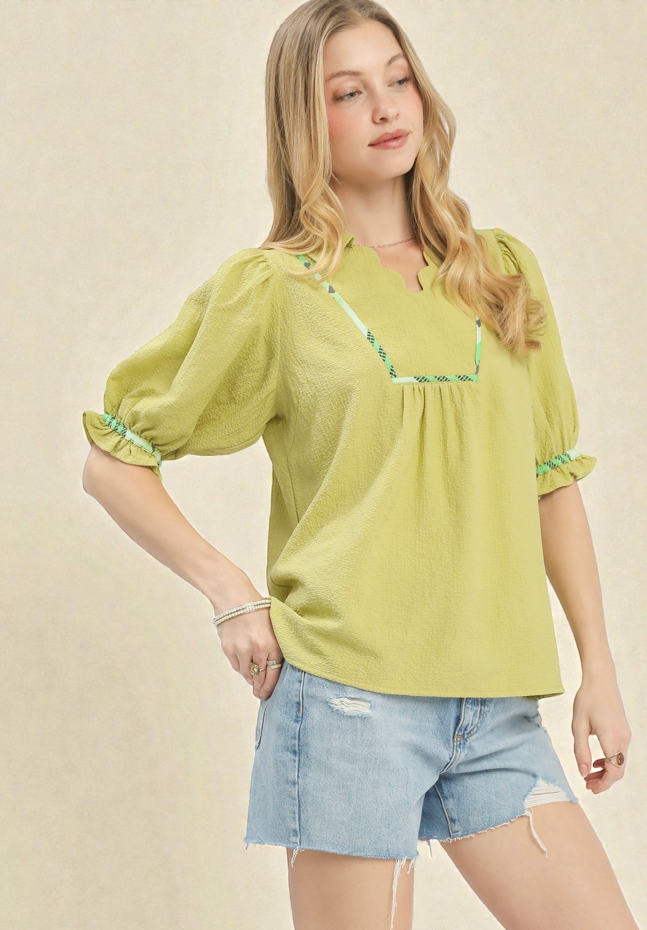 Woman wearing a green blouse with puffed sleeves and denim shorts on a beige background