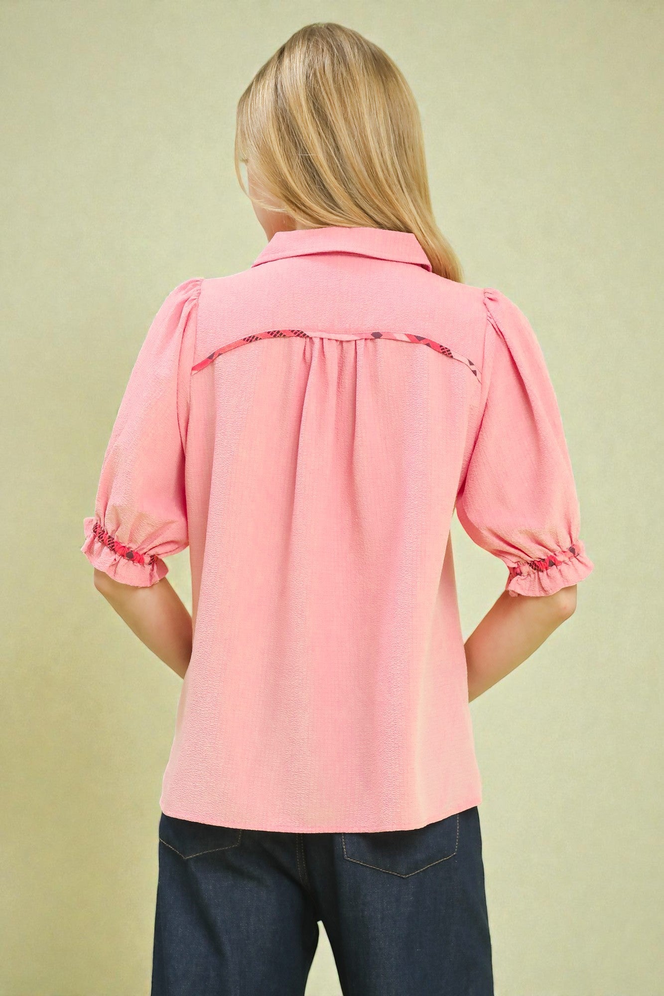 Person wearing a pink blouse with ruffled sleeves on a beige background