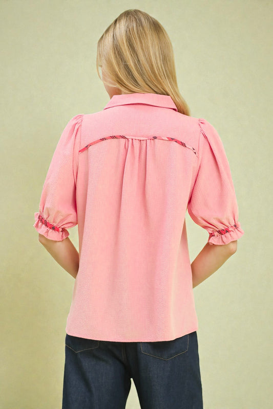 Person wearing a pink blouse with ruffled sleeves on a beige background