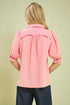 Person wearing a pink blouse with ruffled sleeves on a beige background