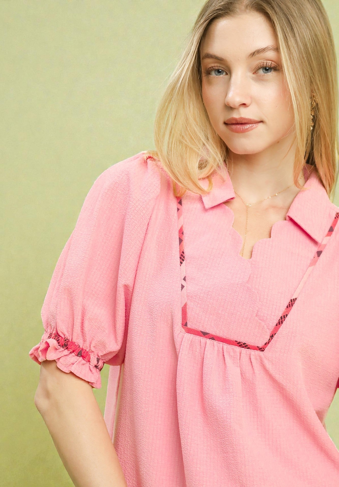 Woman wearing a pink blouse with ruffled sleeves against a light green background