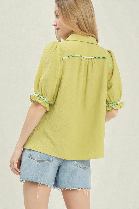 Woman wearing a green blouse with ruffled sleeves and denim shorts on a plain background