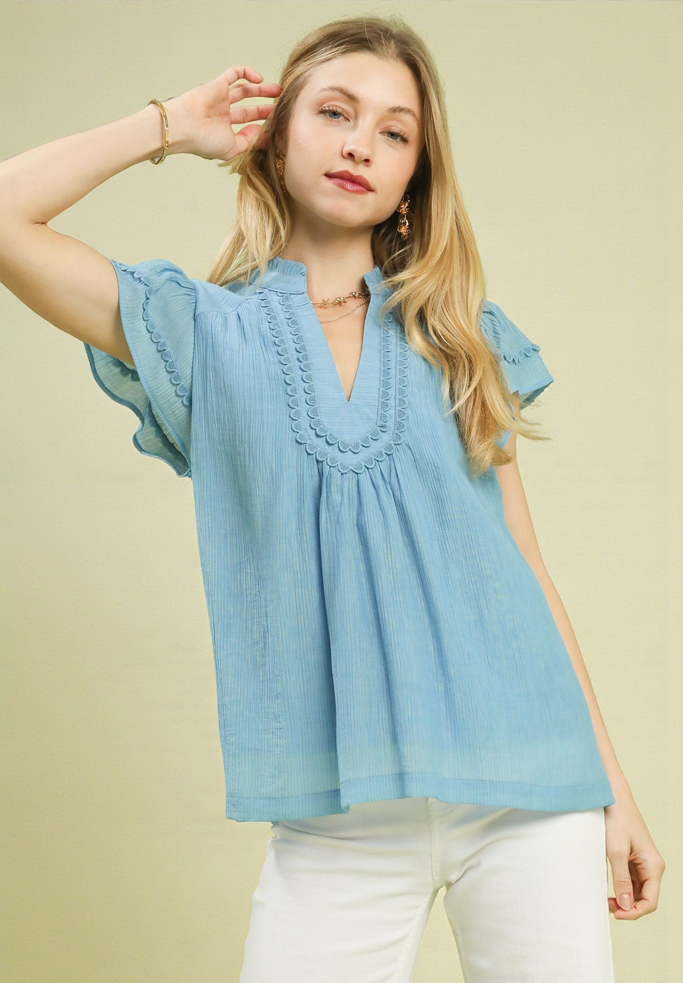 Woman wearing a light blue blouse with ruffled details on a beige background