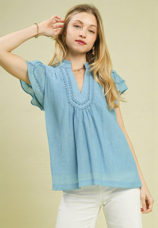 Woman wearing a light blue blouse with ruffled details on a beige background