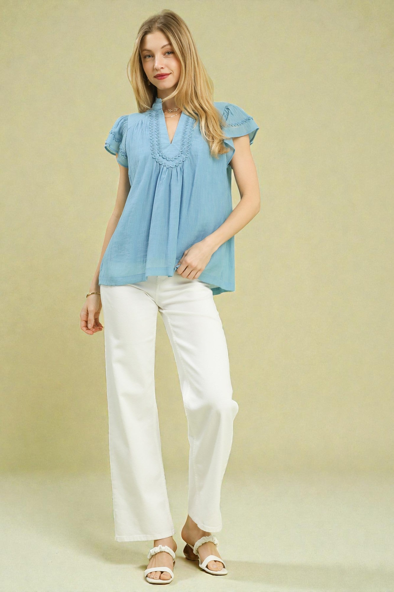 Woman wearing a light blue blouse and white pants on a beige background