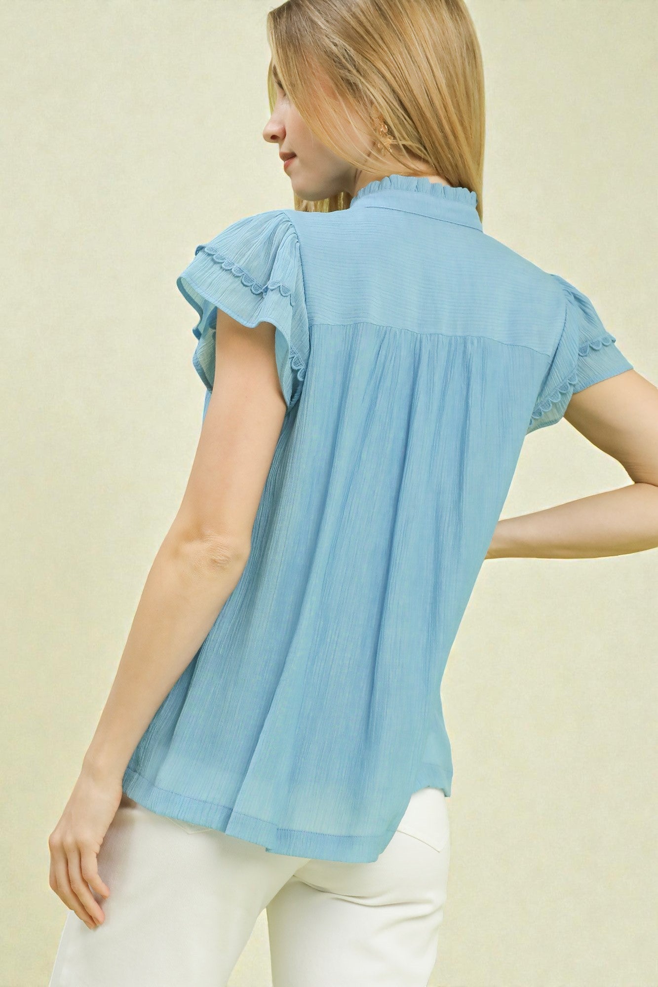 Woman wearing a light blue blouse with ruffled sleeves on a beige background