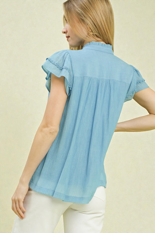 Woman wearing a light blue blouse with ruffled sleeves on a beige background