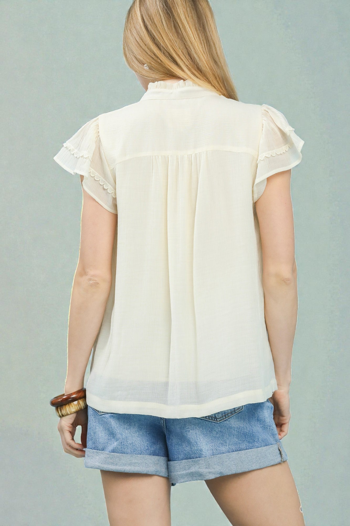 Woman wearing a light-colored blouse and denim shorts against a gray background